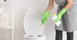 Young woman cleaning toilet in bathroom